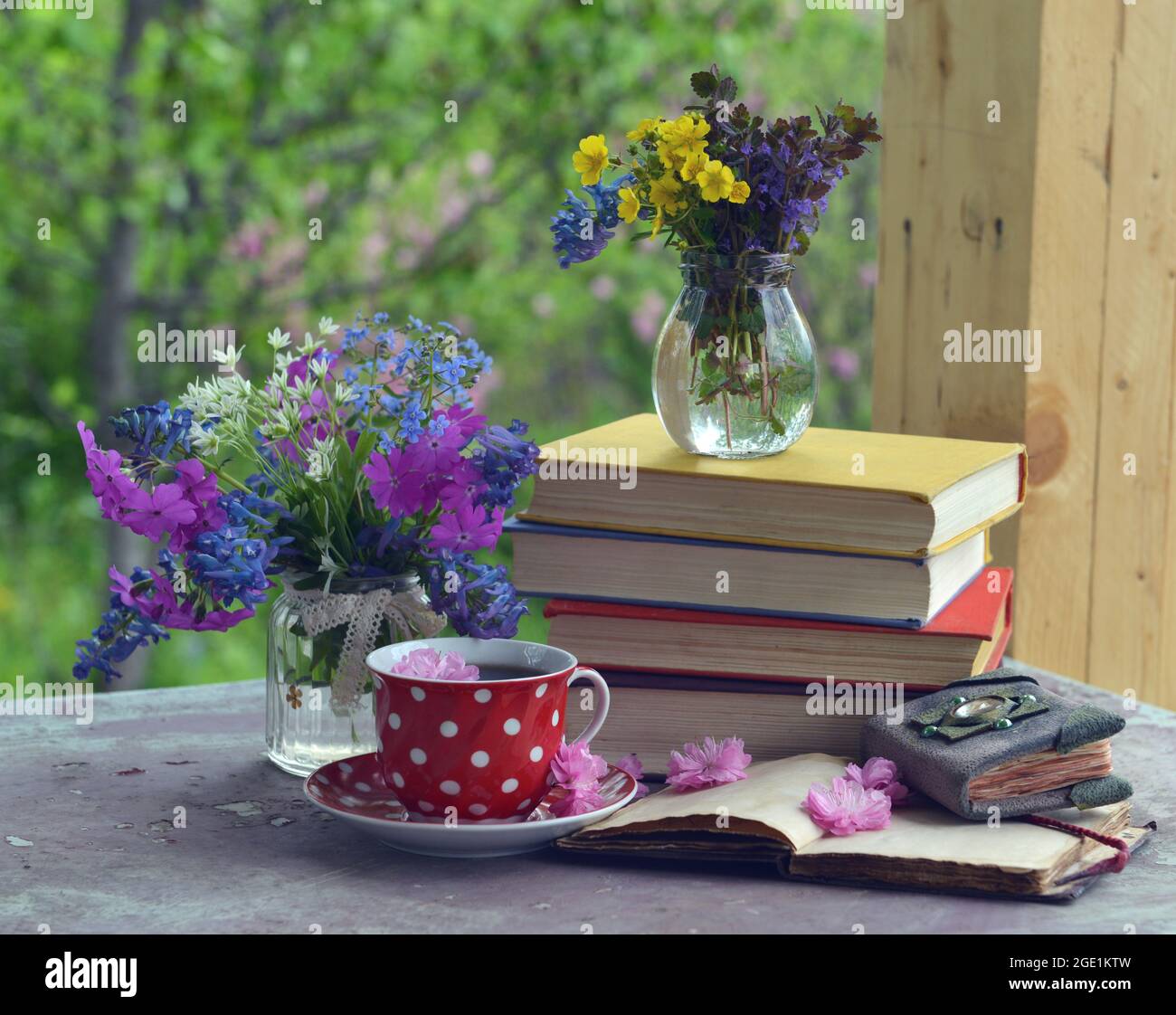 Stillleben mit roter Tasse Tee, Büchern und Frühlingsblumen. Vintage romantisches Konzept draußen im Garten Stockfoto