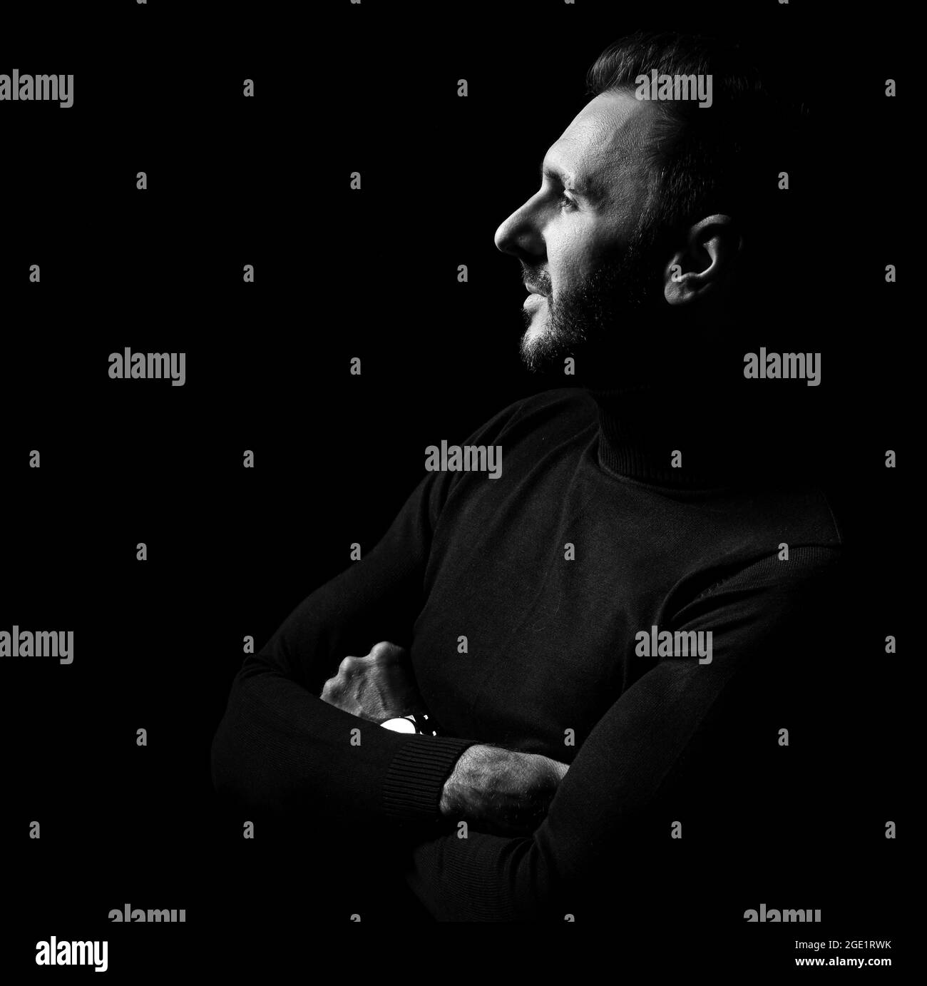 Schwarz und Weiß. Profil eines unrasierten Mannes mit schwarzem Rollkragen, Pullover mit gekreuzten Armen an der Brust Stockfoto