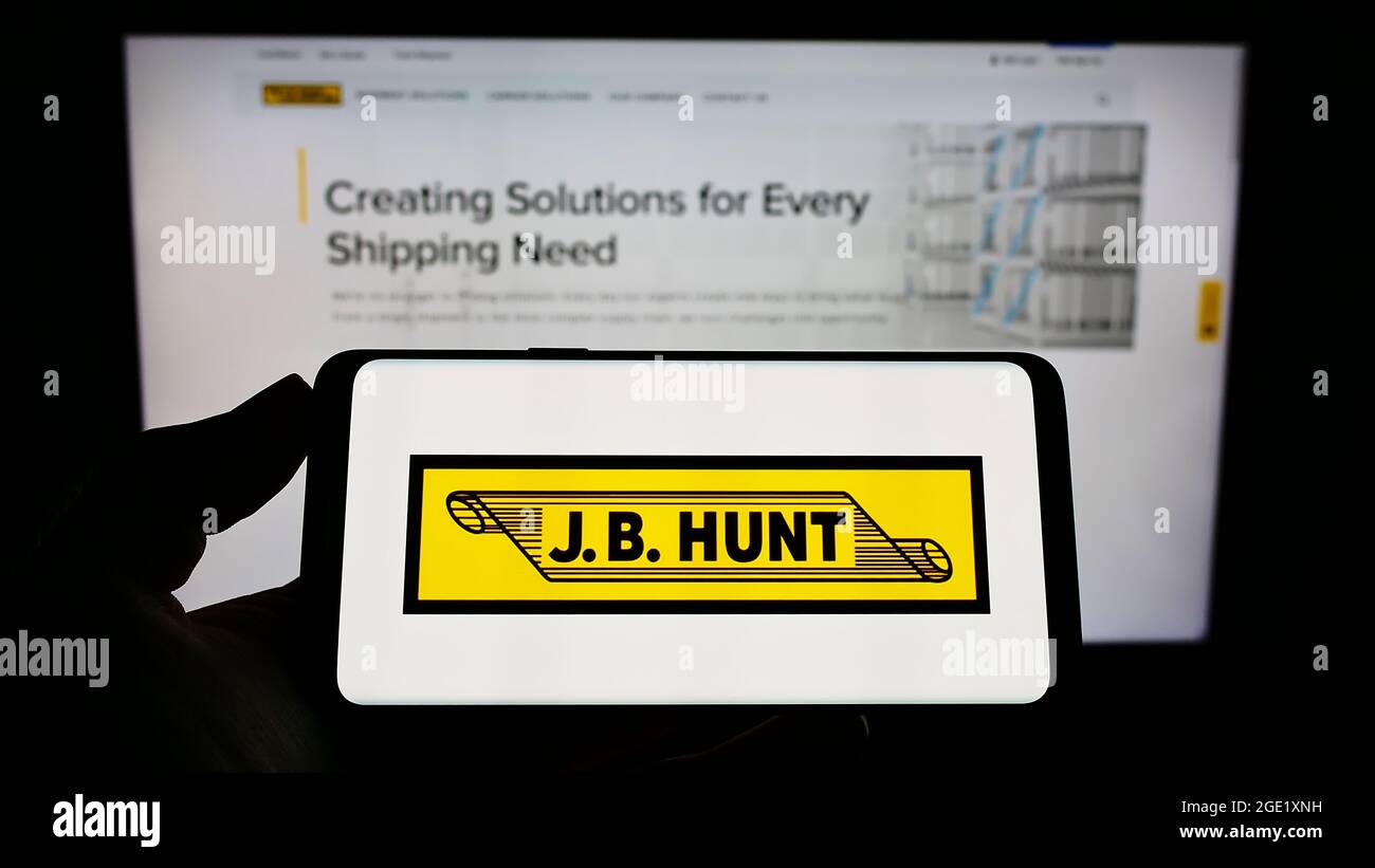 Person, die Mobiltelefon mit Logo des Logistikunternehmens J.B. hält Hunt Transport Services Inc. Auf dem Bildschirm vor der Webseite. Konzentrieren Sie sich auf die Telefonanzeige. Stockfoto