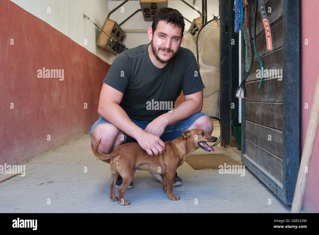Junger latein streichelte seinen Hund und schaute auf die Kamera. Stockfoto