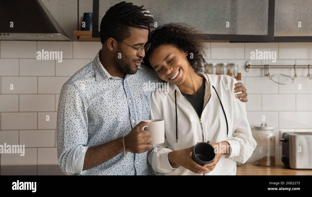 Afrikanisches Liebespaar, das in der modernen Küche mit Kaffeetassen steht Stockfoto