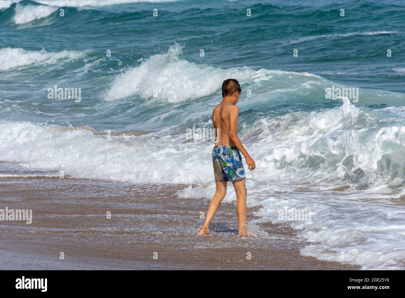 Junger arabischer Junge, der im Meeresschaum am Strand von Jeanne D'Arc, Skikda, Algerien, steht. Stockfoto