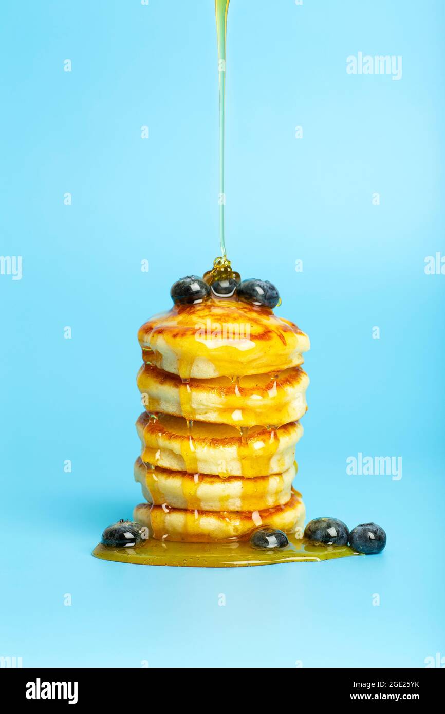 Pfannkuchen mit Beeren auf blauem Banner-Hintergrund. Üppige leckere Pfannkuchen mit Heidelbeeren und Sirup zum Brunch auf einem minimalistisch gefärbten Hintergrund. Schöne helle Lebensmittel Foto. Hochwertige Fotos Stockfoto