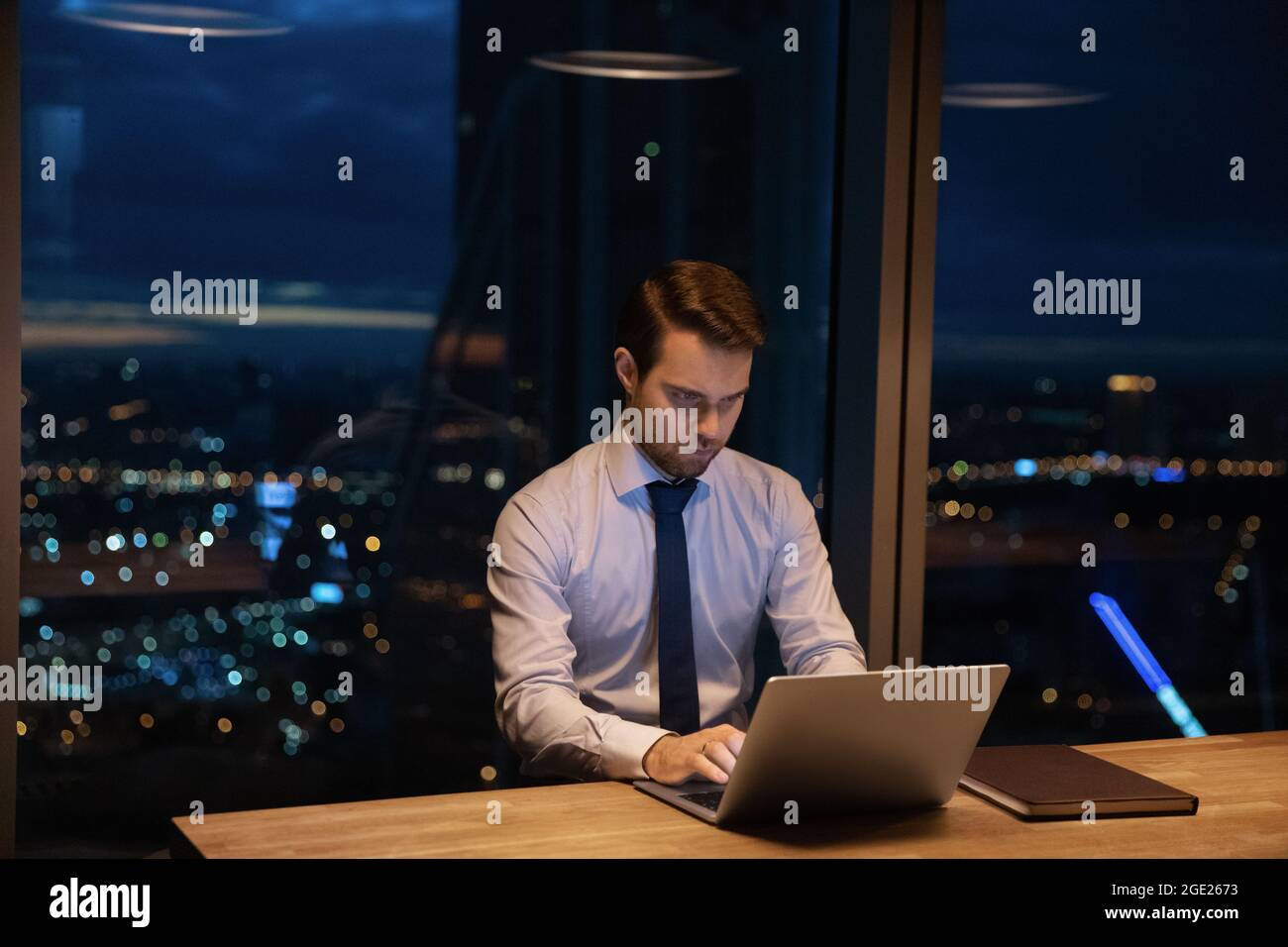 Geschäftsmann sitzt am Arbeitsplatz und arbeitet bis spät in die Nacht mit einem Laptop Stockfoto
