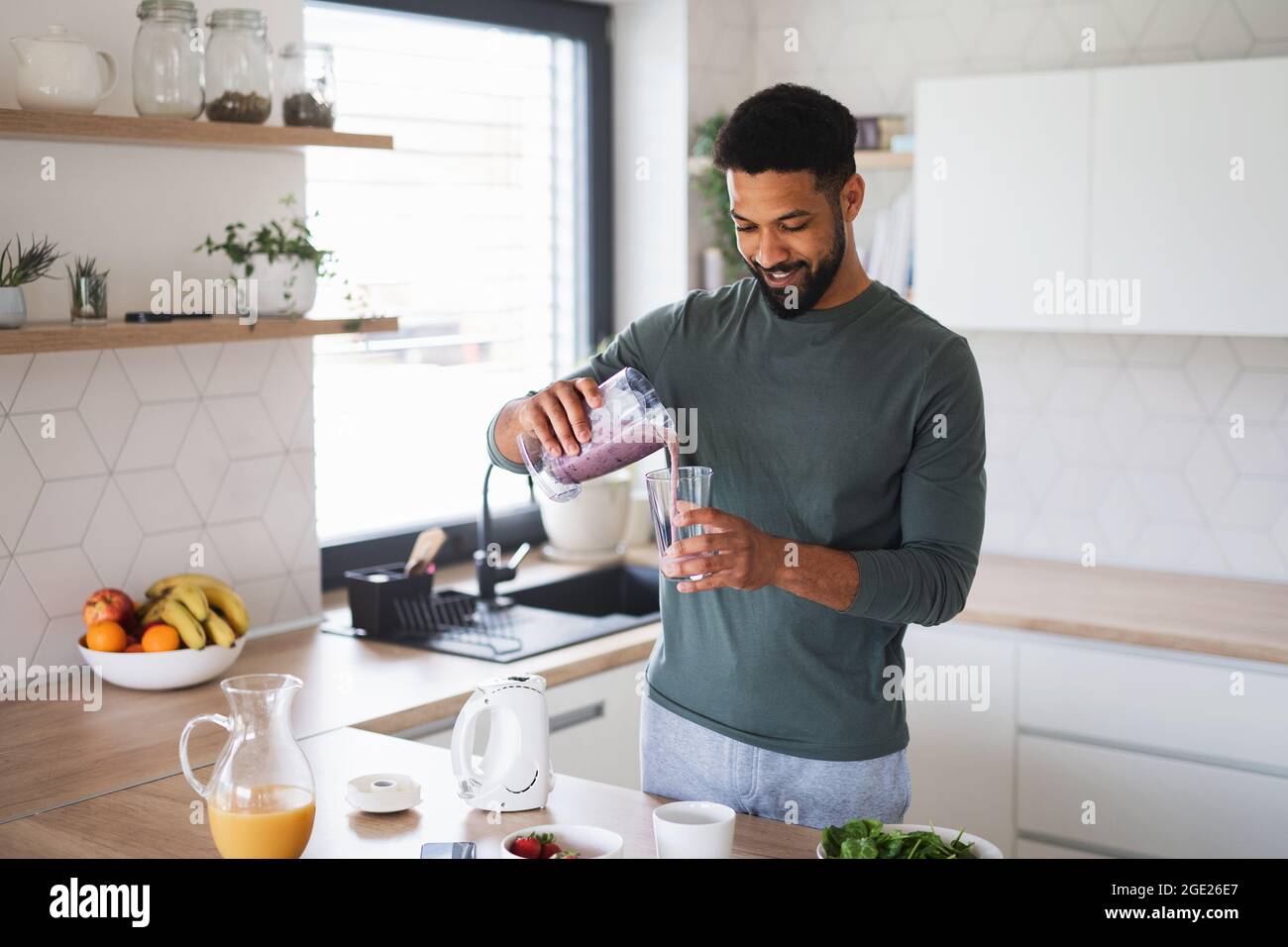 Junger Mann bereitet zu Hause ein gesundes Frühstück zu und gießt Milchshake in Glas. Stockfoto