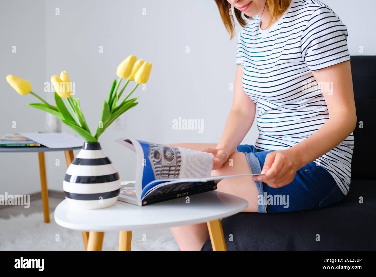 Junge Frau liest einen Katalog oder ein Reisemagazin und wählt in einem schönen, modernen Wohnzimmer ein Reiseziel für die Reise aus Stockfoto
