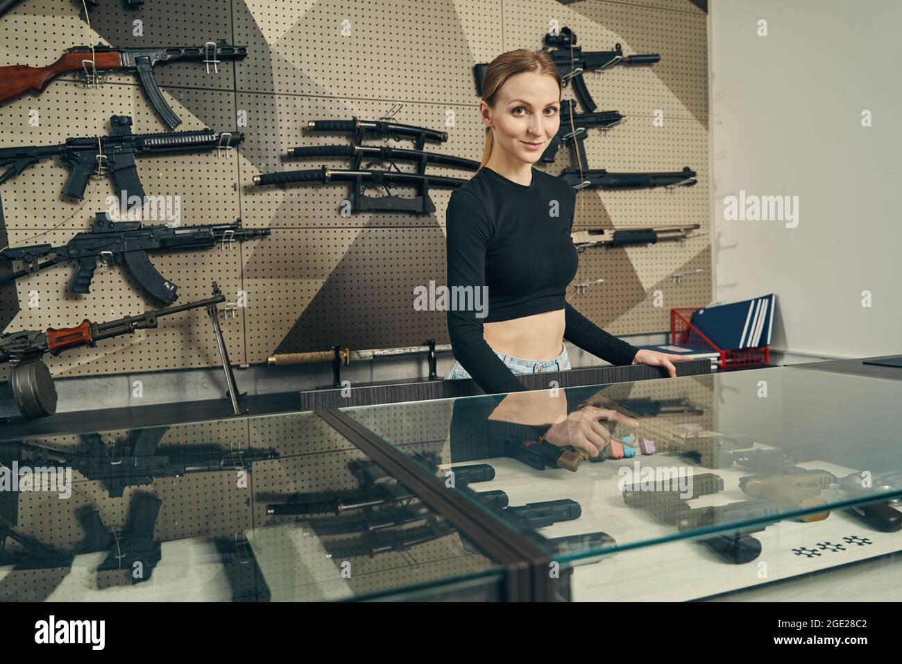Junge Verkäuferin posiert im Waffenladen für die Kamera Stockfoto