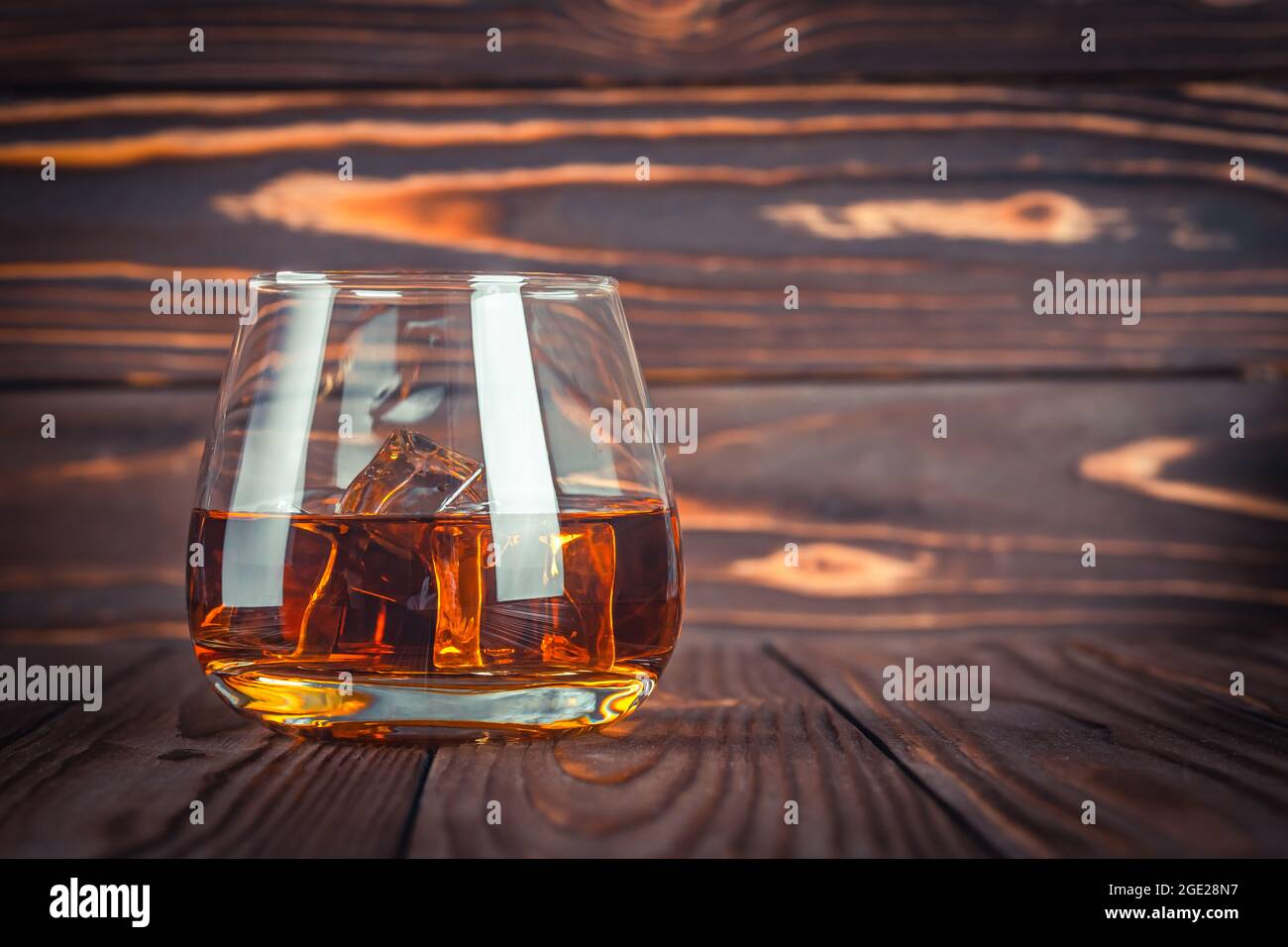 Glas Whiskey mit Eis, Brandy auf einem dunkelbraunen Holztisch. Bourbon. Starker Alkoholkonsum aus nächster Nähe. Rum, Scotch. Stillleben im rustikalen Stil Stockfoto