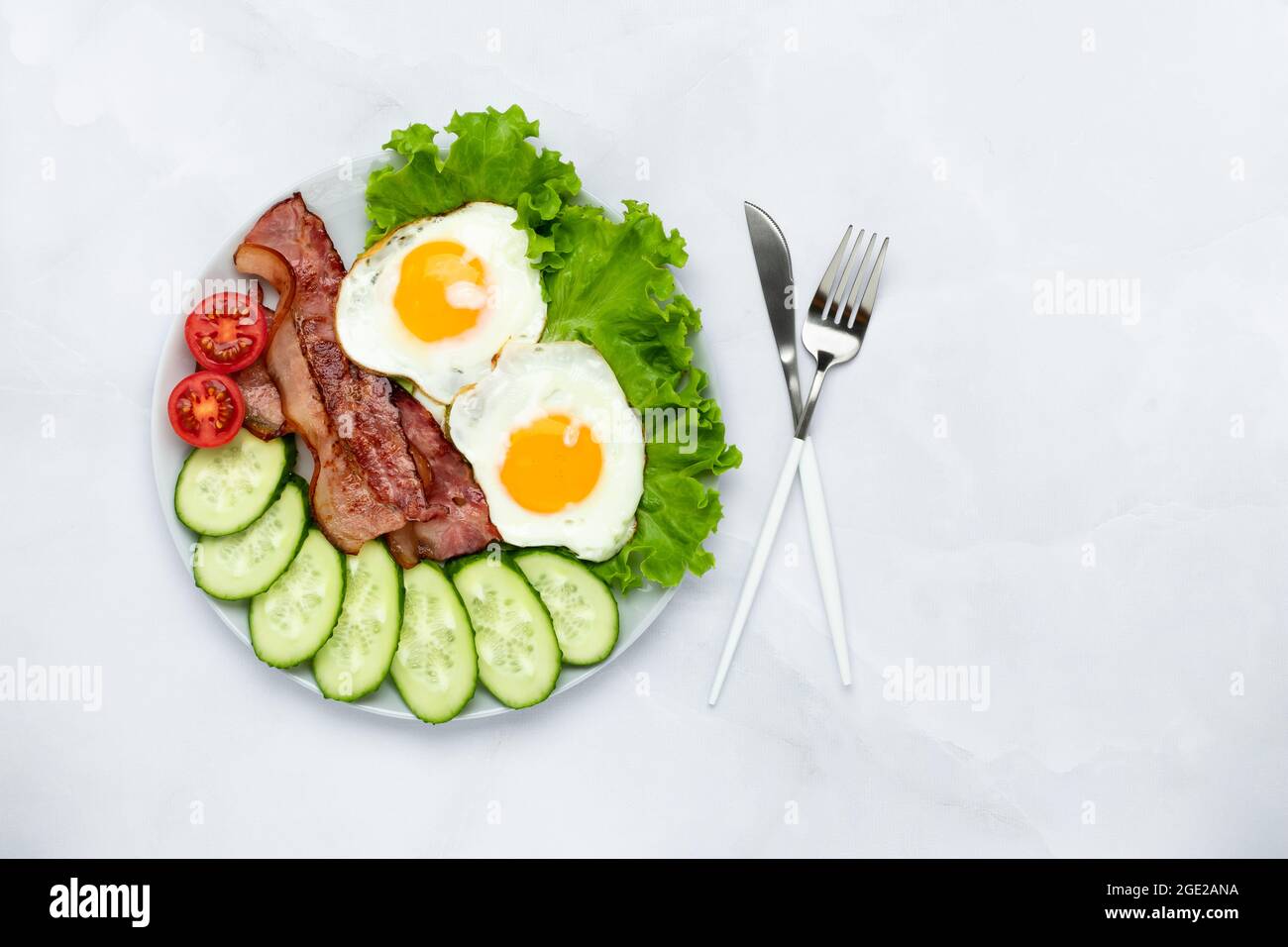 Gebratene Hühnereier mit Speck und Gemüse auf einem grauen Tisch. Frühstückskonzept. Draufsicht. Das Essen am Morgen. Frisch geschnittene Gurken und Toma Stockfoto