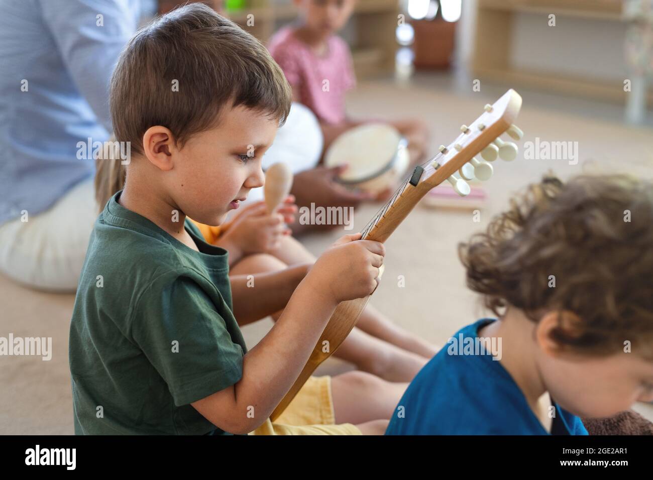 Gruppe von kleinen Kindergartenkindern, die im Klassenzimmer auf dem Boden sitzen und Musikinstrumente spielen. Stockfoto