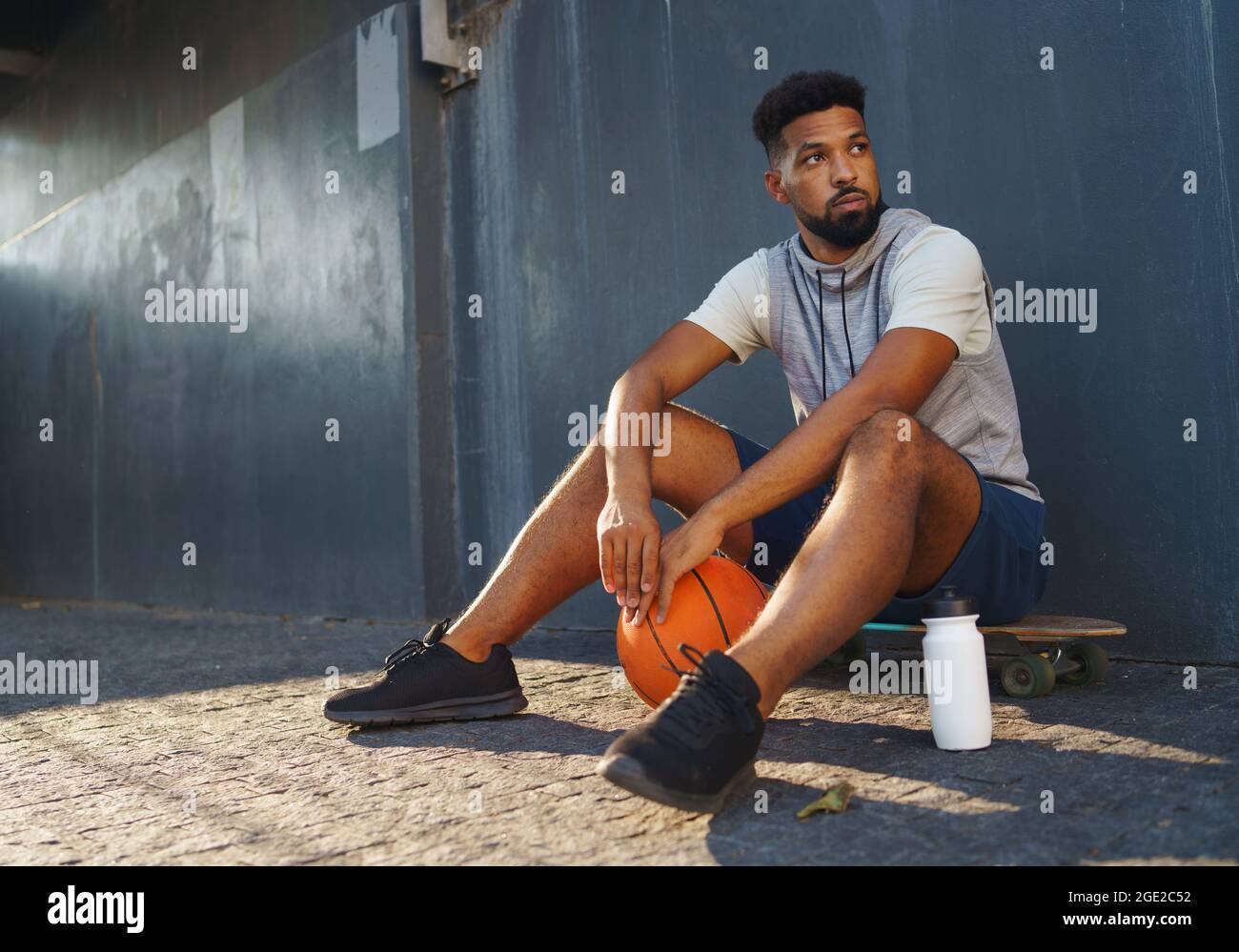 Trauriger junger Mann mit Basketballball im Freien in der Stadt, sitzend und ausruhend. Stockfoto