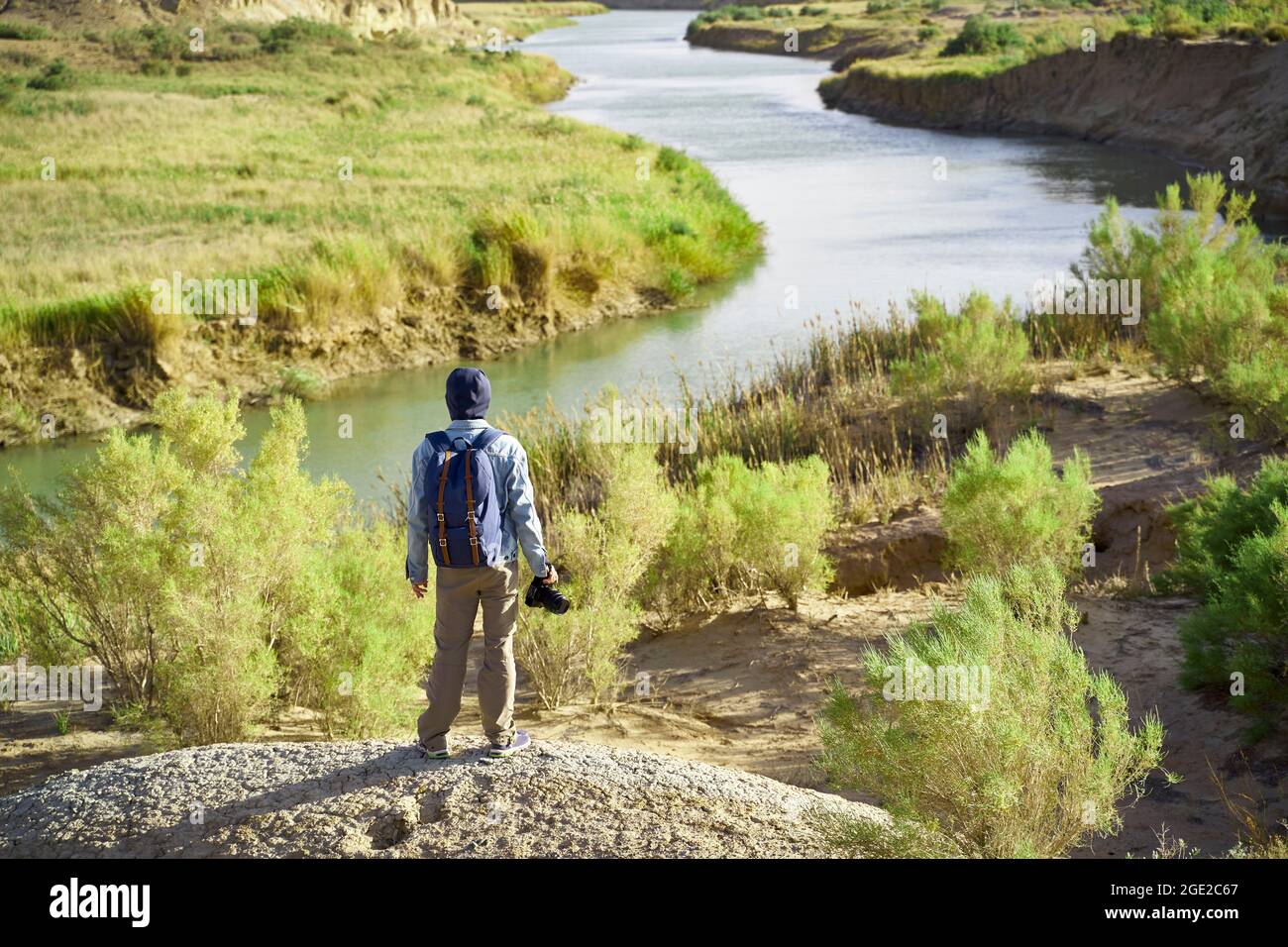 Rückansicht eines männlichen asiatischen Fotografen, der auf einem Hügel steht und auf einen Fluss blickt Stockfoto