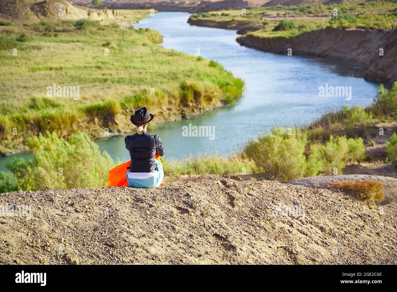 Rückansicht einer asiatischen Frau, die auf einem Hügel sitzt und auf die wunderschöne Flusslandschaft blickt Stockfoto