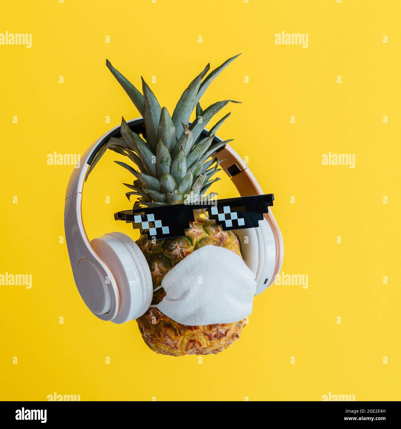 Kreative lustige Ananas Gesicht trägt Brille Kopfhörer und schützende medizinische Maske. Ruhende schwebender Ananas Gesicht auf Farbe gelb Sommer Stockfoto