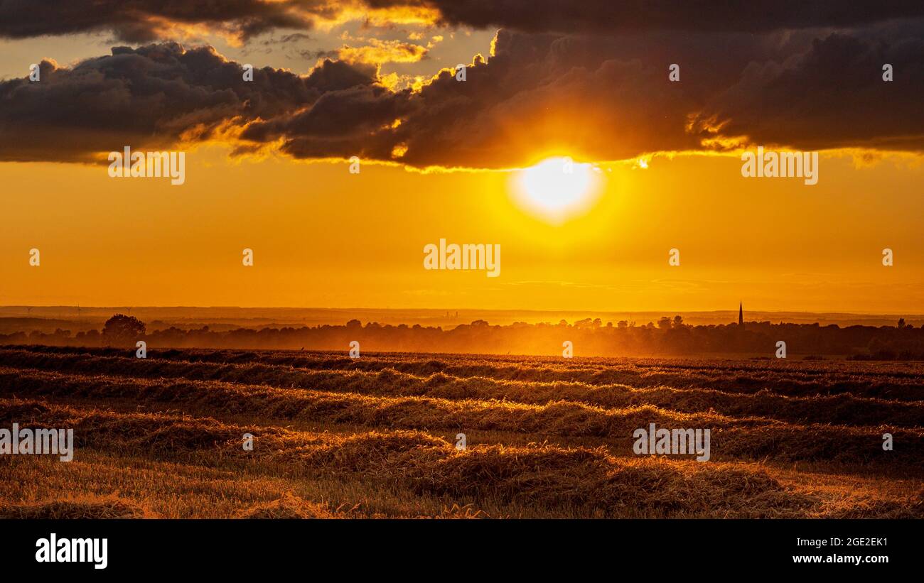 Caythorpe, Lincolnshire, Großbritannien. Sonnenuntergang während der Erntezeit auf einem Stoppelfeld mit Blick auf das Dorf Stockfoto