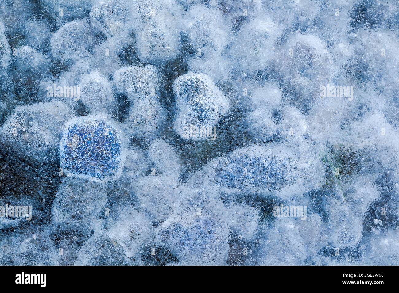 Eisverkapselung kleiner Steine und Luftblasen, die einen mehrfarbigen und stark texturierten Effekt erzeugen Stockfoto