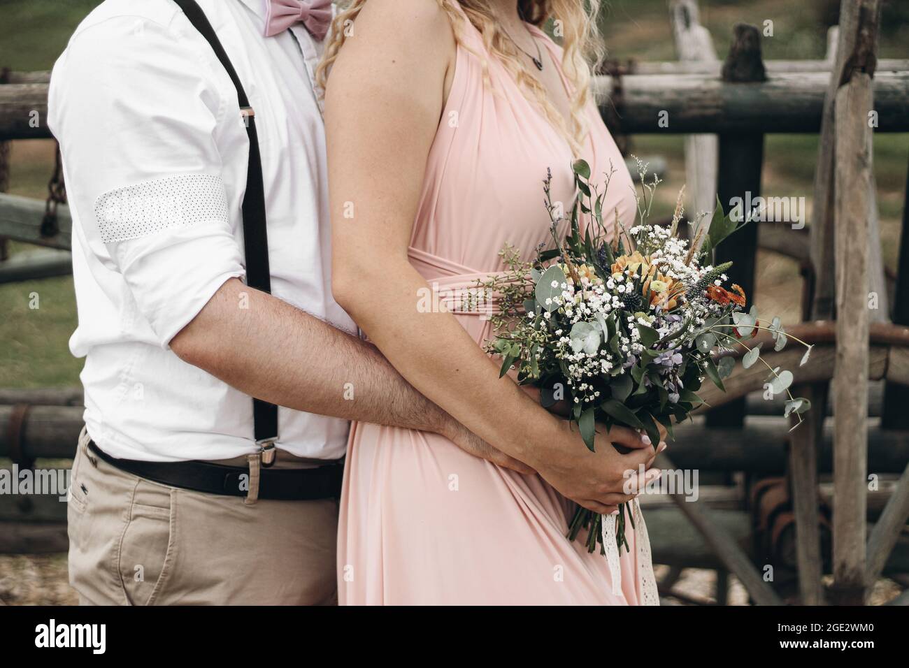 Nahaufnahme des Bräutigams, der eine Braut in einem wunderschönen rosa Kleid umarmt. Frau mit Blumenstrauß in den Händen. Boho Hochzeit und Ehe Komposition. Engagement Stockfoto