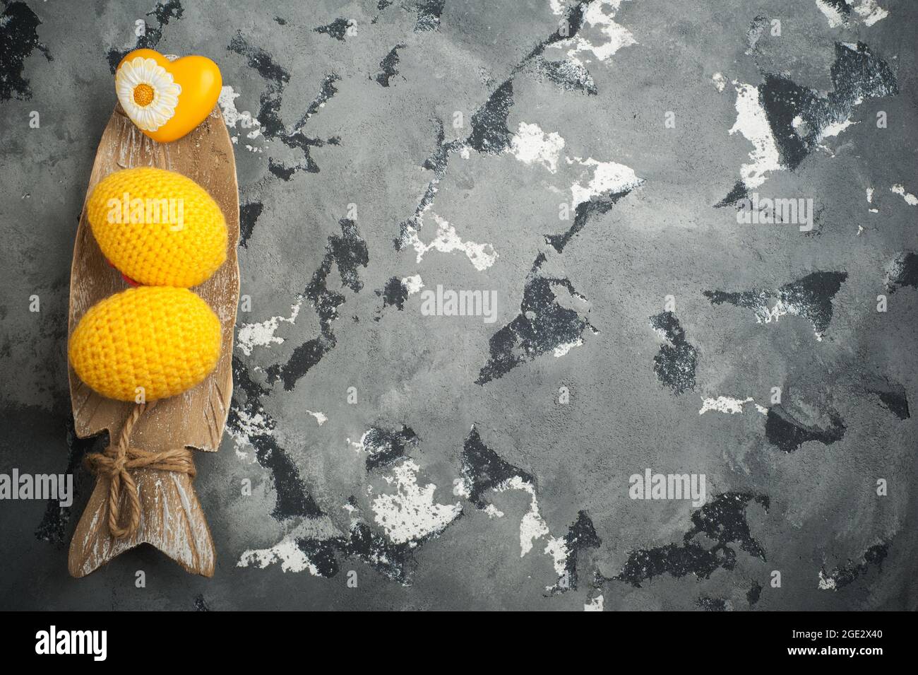 Gelbe gehäkelte ostereier und Herz auf betontem Hintergrund. Skandinavische Einrichtung, Ostern oder Valentinstag. Copyspace für Text Stockfoto