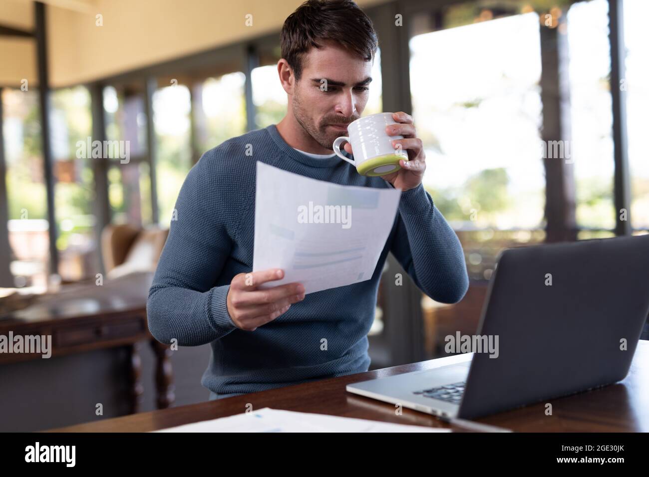 Kaukasischer Mann, der am Tisch sitzt und ferngesteuert mit einem Laptop arbeitet Stockfoto