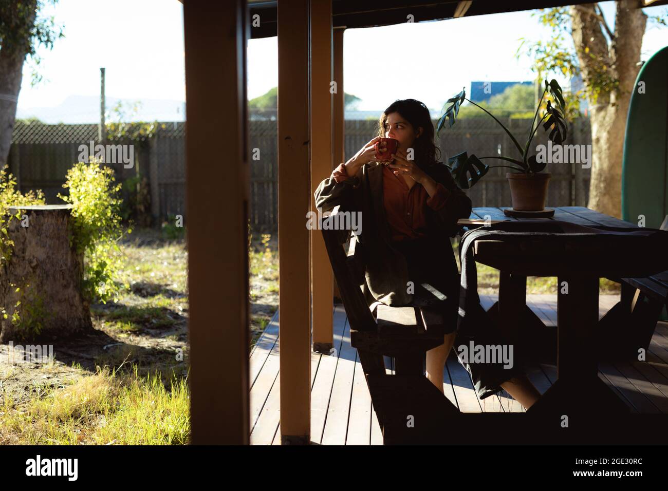 Frau mit gemischter Rasse, die im sonnigen Garten sitzt und Kaffee trinkt Stockfoto