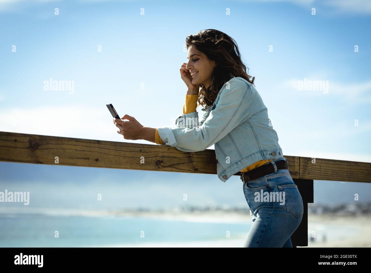 Frau mit gemischtem Rennen am sonnigen Tag am Meer mit dem Smartphone Stockfoto