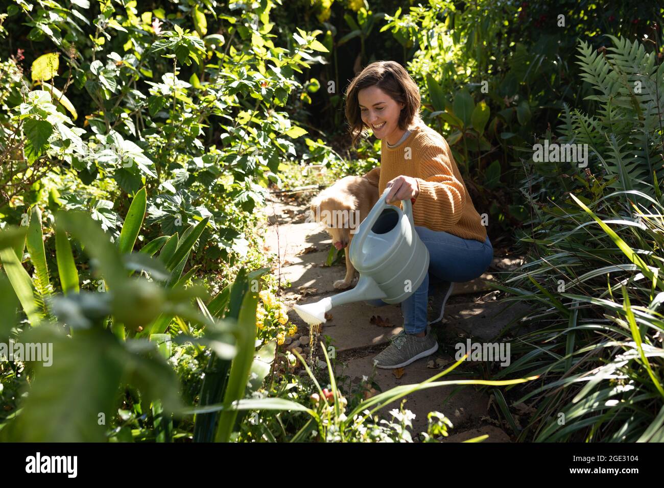 Lächelnde kaukasische Frau im Garten mit ihrem Hund, Gartenarbeit Stockfoto