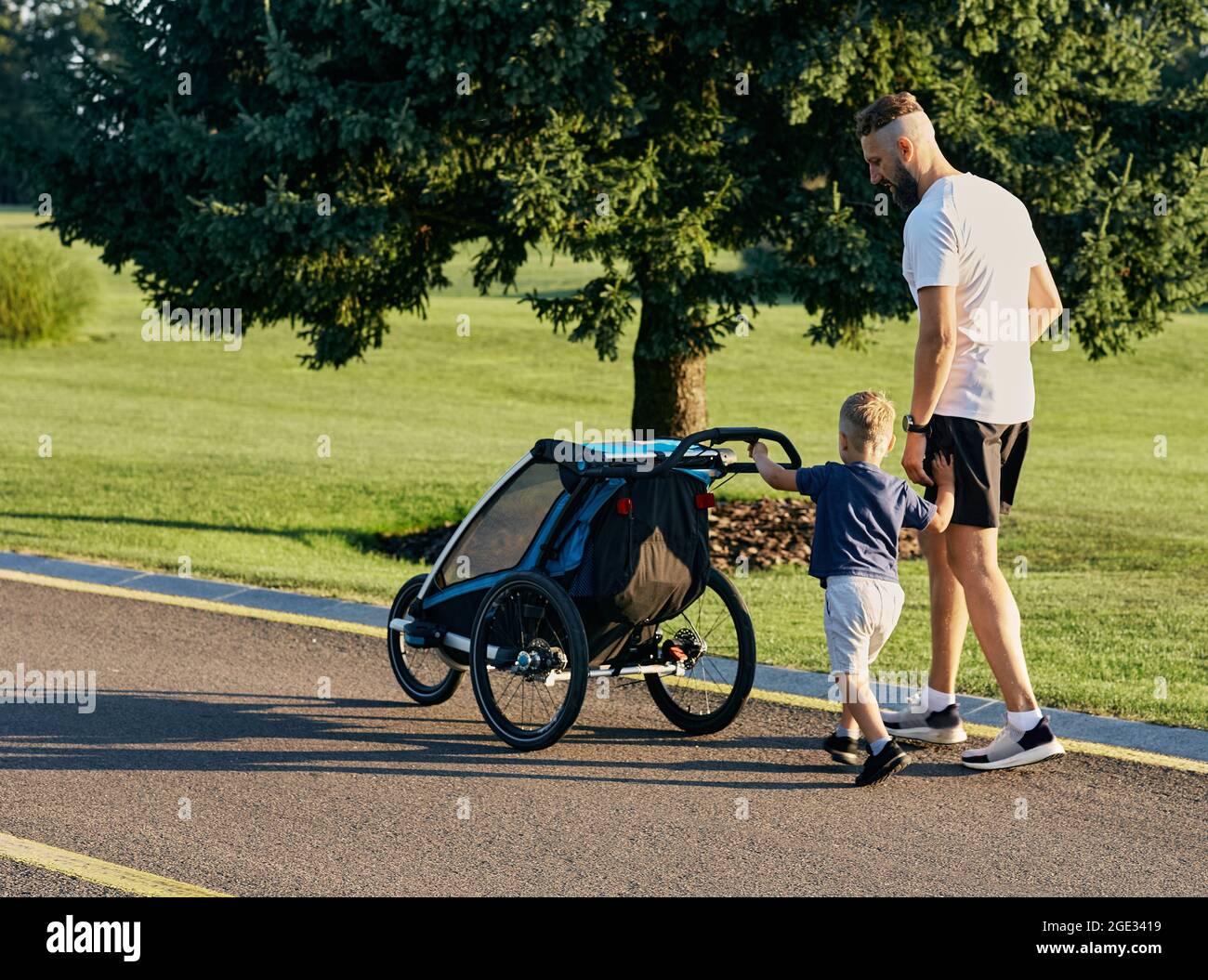 Vater und sein kleiner Sohn gehen gemeinsam im Stadtpark und schieben eine Babykutsche. Vaterschaft, Papa und Kind. Vatertag Stockfoto