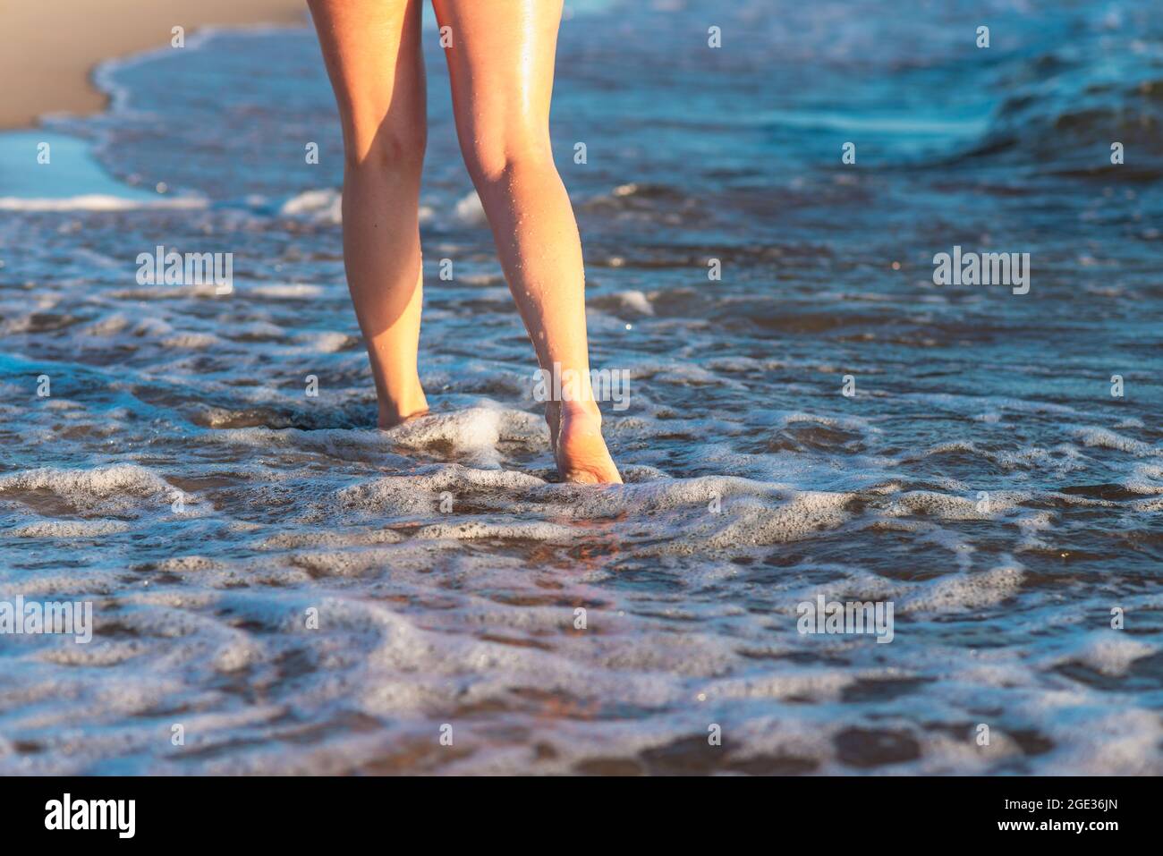 Frau Beine und Füße, die auf dem Sand des Strandes mit dem Meerwasser im Hintergrund zu Fuß auf dem Strand. Nahaufnahme von Beinen, die am Meer entlang laufen Stockfoto