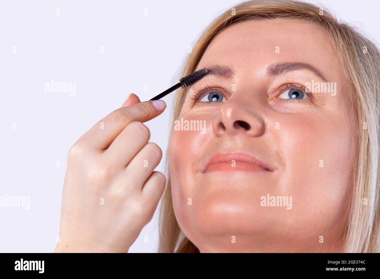 Kaukasische hübsche Frau mit brillantem Gesichtston tut Verfahren zum Kämmen der Augenbrauen mit einem Pinsel in einem Schönheitssalon. Stockfoto