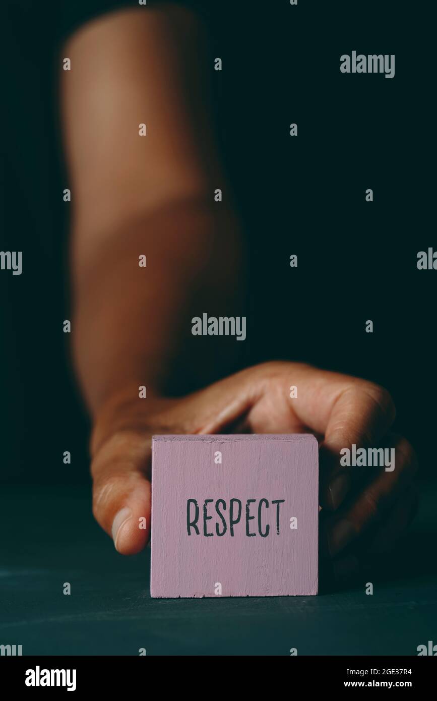 Nahaufnahme eines jungen kaukasischen Mannes, der einen pinkisch-violetten Baustein mit dem darin geschriebenen Text Respect auf einer dunkelgrauen Oberfläche zeigt Stockfoto
