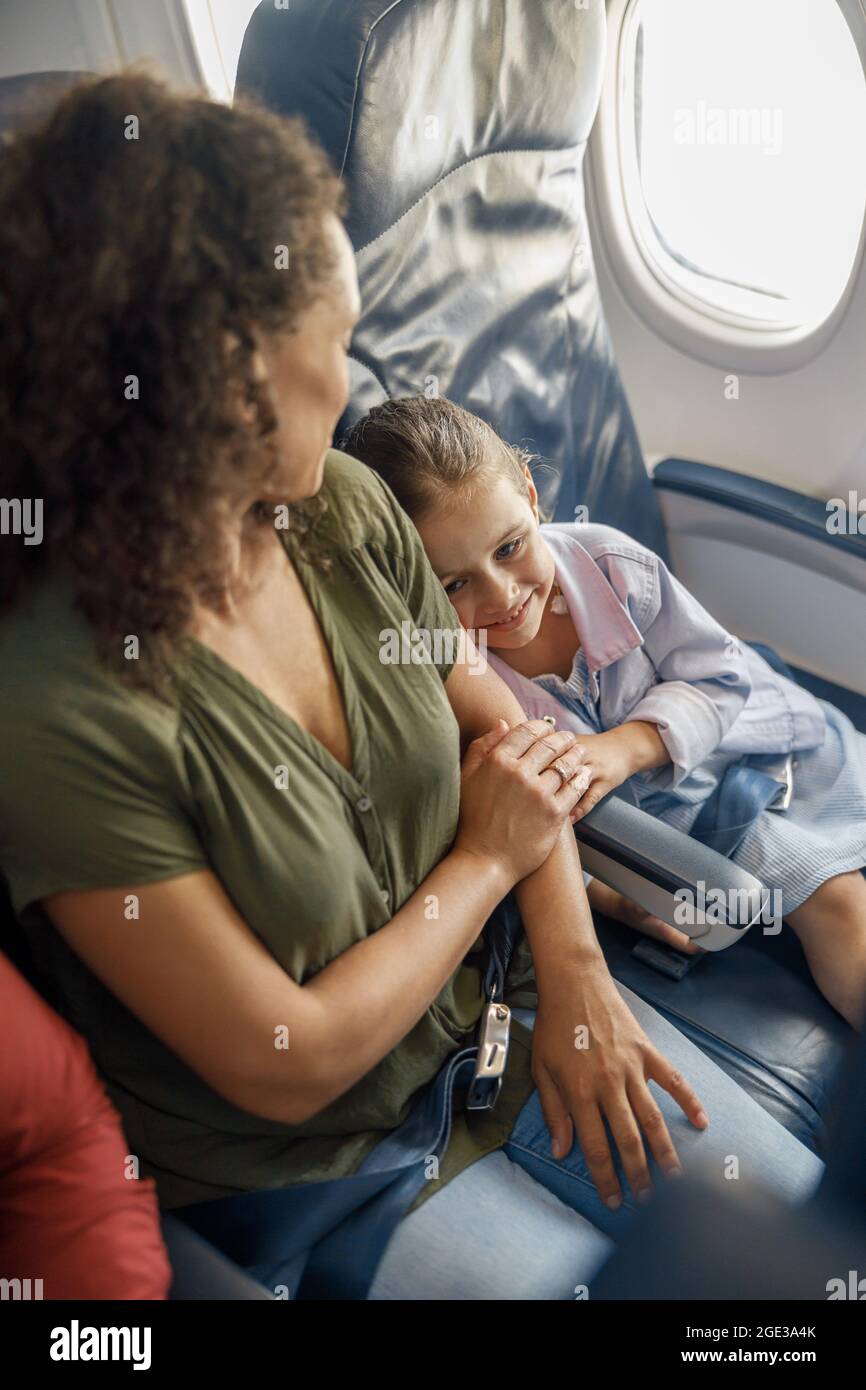 Blick in die Höhe des kleinen Mädchens, das im Flugzeug sitzt und sich auf ihre Mutter lehnt, während sie zusammen reist Stockfoto