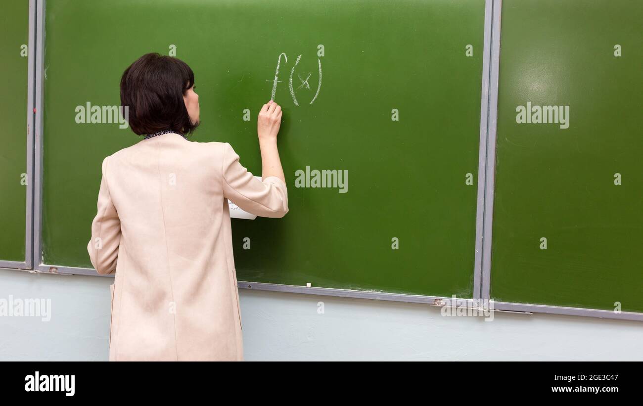 Eine Lehrerin schreibt mathematische Formel auf einer Tafel. Stockfoto