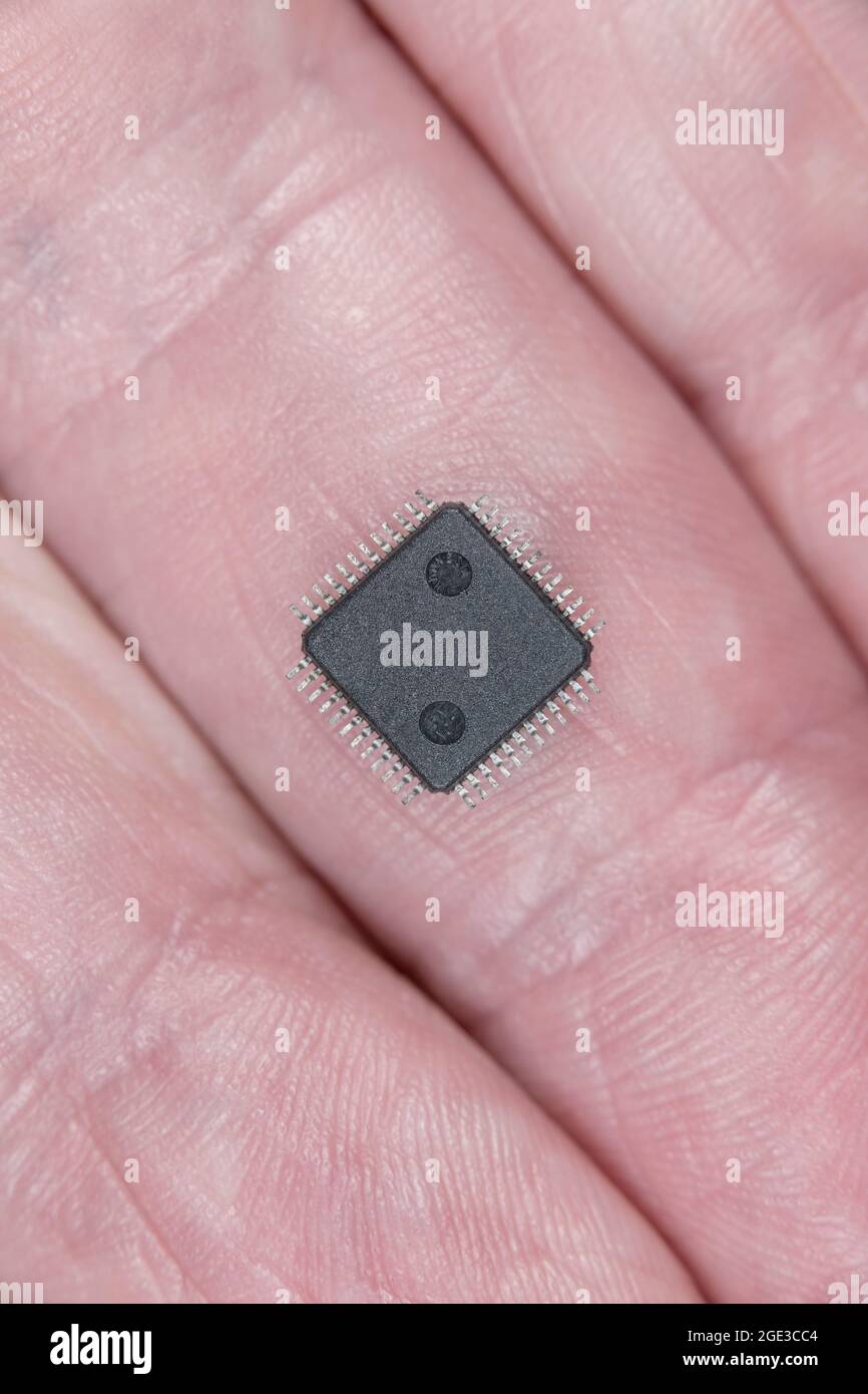 Nahaufnahme Unterseite des kleinen IC/integrierten Schaltungs-Chips an den Fingern mit winzigen Bauteilgrößen und Flügelbeinen. Dies ist ein MP3-/WMA-Audio-IC. Stockfoto