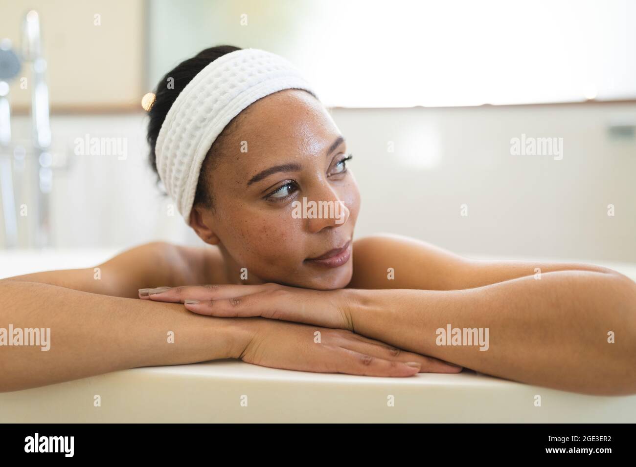 Lächelnde Frau mit gemischter Rasse im Badezimmer, die sich im Bad entspannt Stockfoto