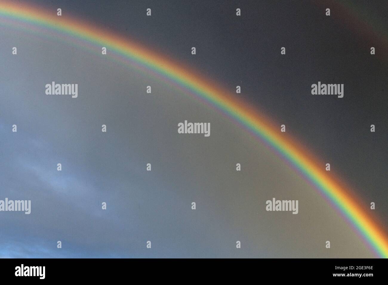 Einzelner Regenbogen, der sich in einen dunklen und düsteren Himmel überspannt Stockfoto