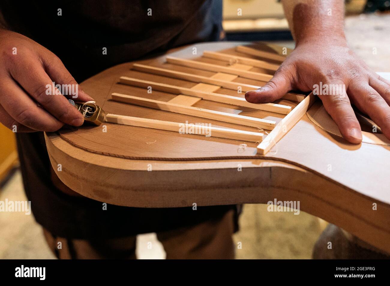 Unanerkannter Handwerker, der eine Gitarre kreiert und Werkzeuge in einer traditionellen Werkstatt verwendet. Stockfoto