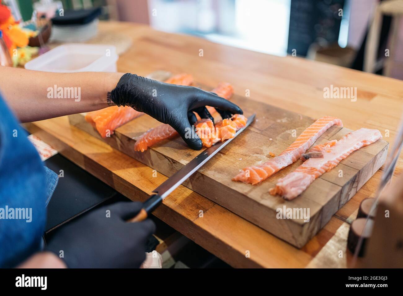 Nicht anerkannter Restaurantmitarbeiter trägt Latexhandschuhe und schneidet Lachs mit einem Messer. Stockfoto