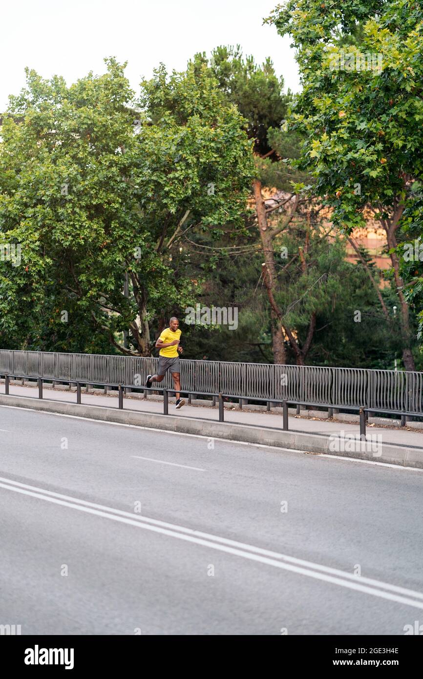 Fernansicht eines afroamerikanischen Sportlers mit gelbem T-Shirt und Shorts, die draußen auf dem Bürgersteig in der Stadt sprinten. Stockfoto
