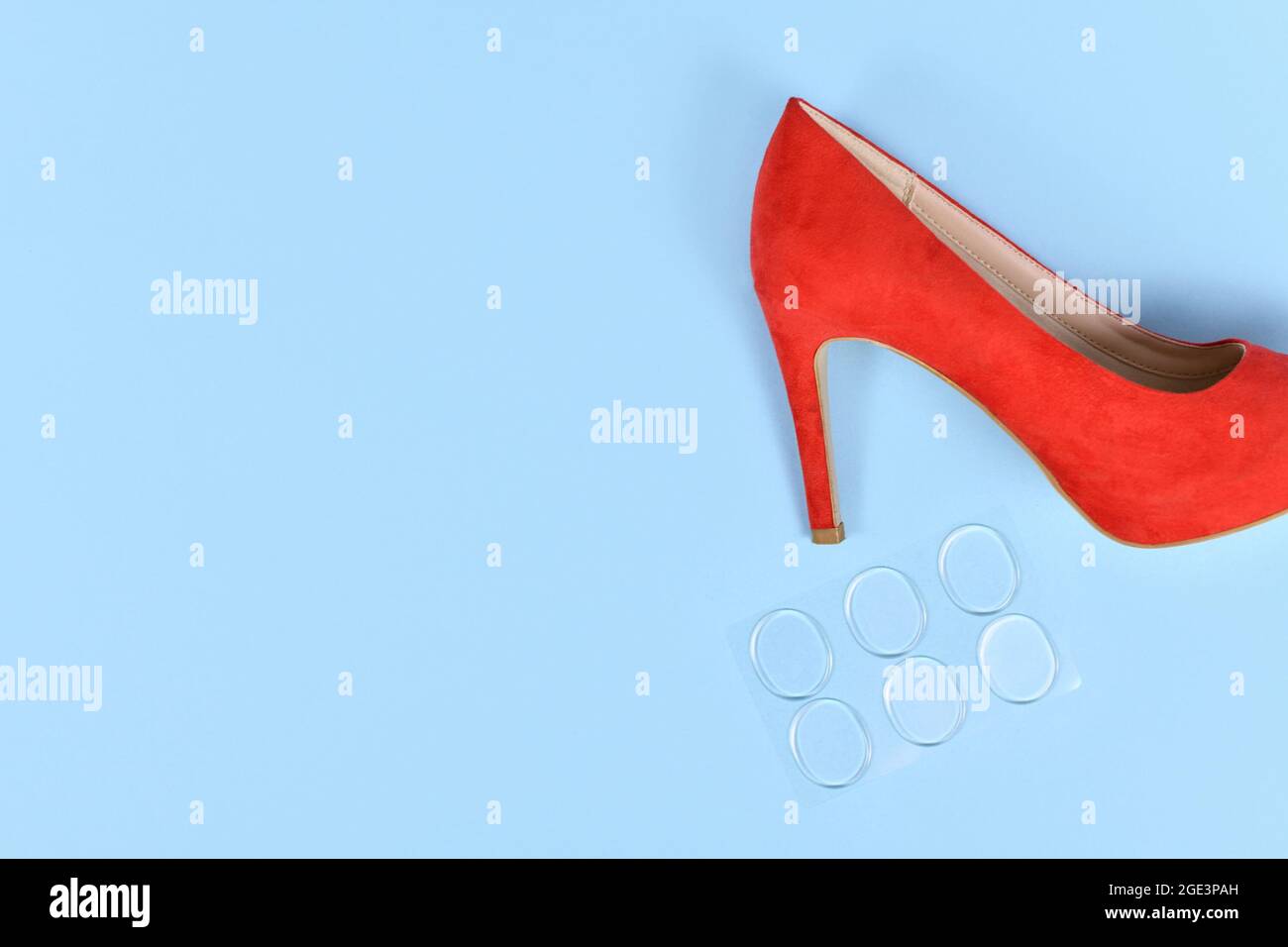 Schuh-Einlegesohlenschutz-Gel-Aufkleber zur Entlastung von Druckpunkten neben rotem hohem Absatz auf blauem Hintergrund mit Kopierraum Stockfoto