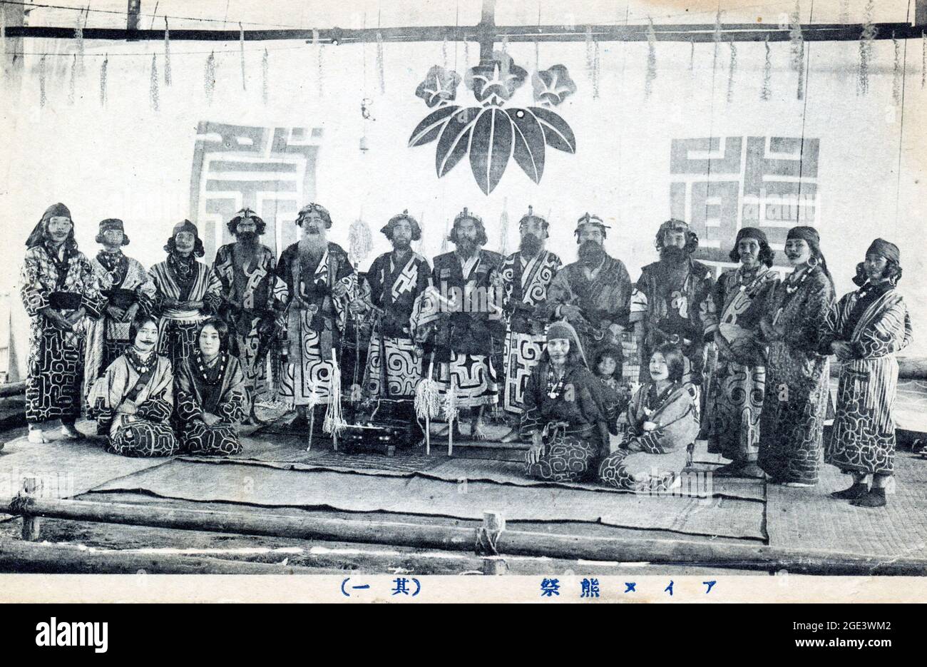 Alte japanische Schwarz-Weiß-Postkarte, um 1910, von einer Gruppe von Ainu-Leuten in formeller Pose, stehend und knieend, in traditioneller Tracht. Stockfoto