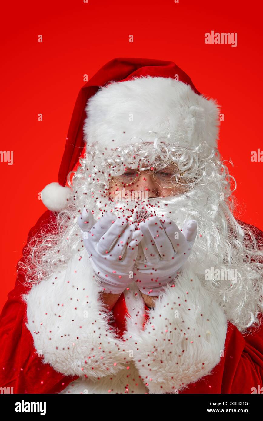 weihnachtsmann bläst rote Glitzer-Konfetti aus den Händen Stockfoto