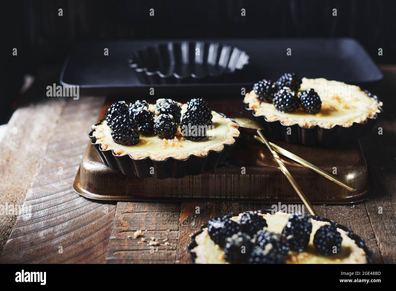 Frisch gebackene Minitörtchen mit Brombeeren auf einem Holztisch. Stockfoto