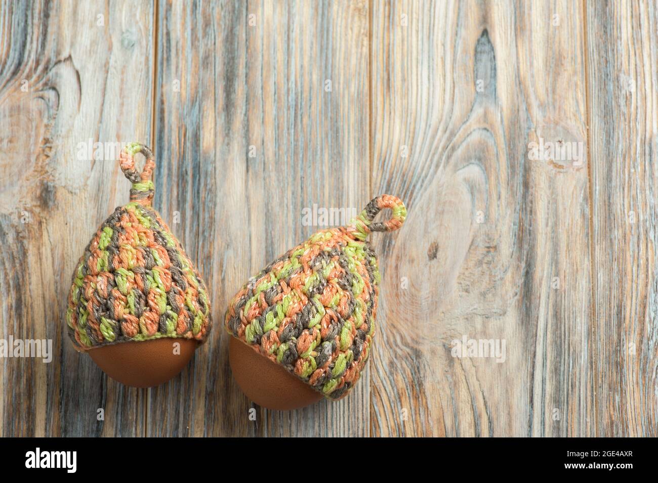 Osterkomposition mit Eiern in gestrickten Hüten auf einem Holztisch. Stockfoto