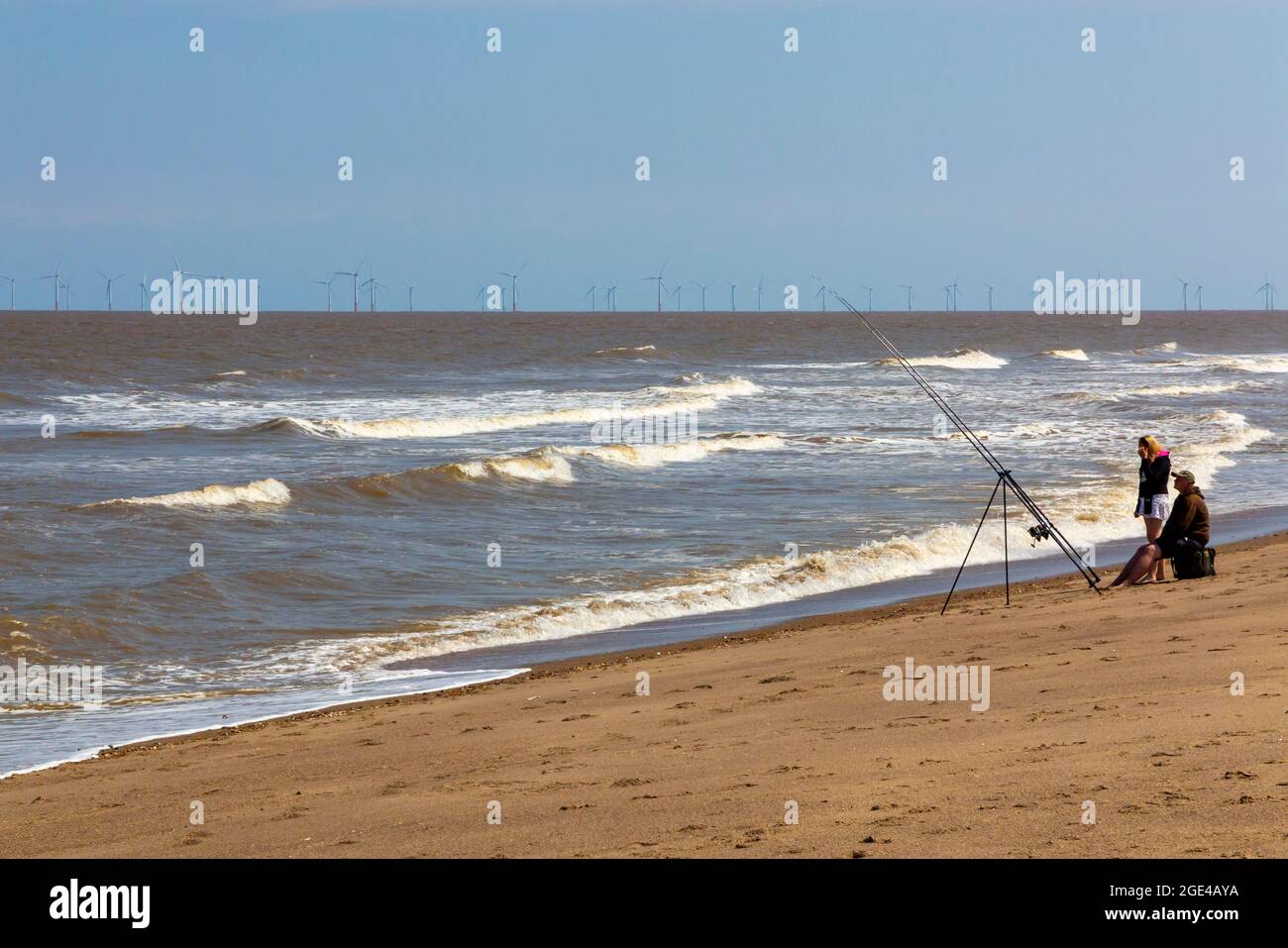 Menschen Seefischen am Sandstrand von Chapel St Leonards in Lincolnshire, England, mit Offshore-Windpark-Turbinen am Horizont sichtbar. Stockfoto