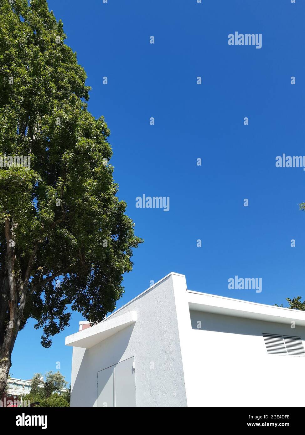 Weißes Gebäude vor blauem Himmel mit grünem Baum an einer Tankstelle, Olivais in Lissabon, Portugal Stockfoto