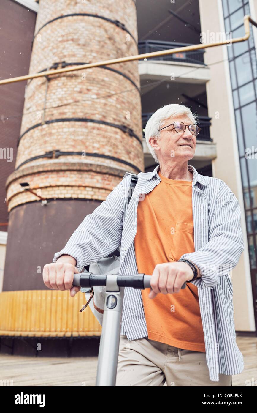 Vertikale Taille bis Porträt von aktiven Senior Mann Reiten Elektroroller im Freien und Blick weg in der Stadt Stockfoto