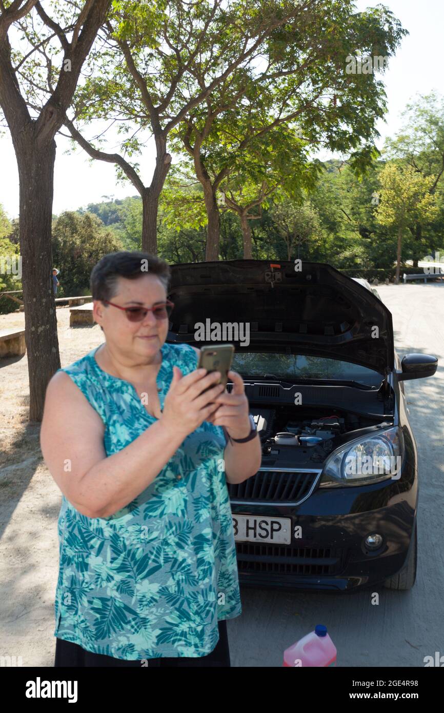 Frau, die mit dem Mobiltelefon die Pannenhilfe vor einem offenen Auto mit Motor in Sicht anruft Stockfoto