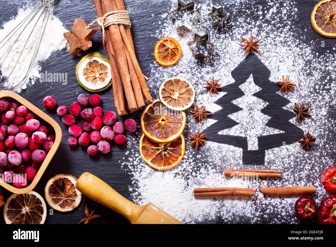 Weihnachtsküche: Tannenbaum aus Mehl auf dunklem Tisch, Backzutaten, gefrorene Preiselbeere und getrocknete Früchte auf dunklem Grund, Draufsicht Stockfoto