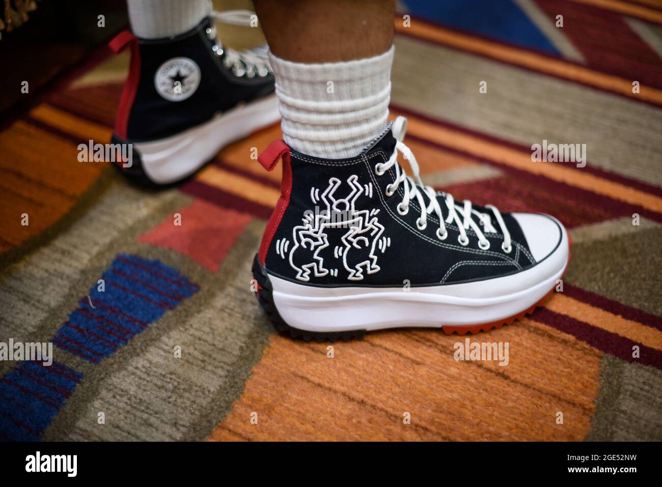 Ein junger Mann trägt ein Paar Converse High-Top-Sneakers, die mit Zeichnungen des Künstlers Keith Haring verziert sind. Stockfoto