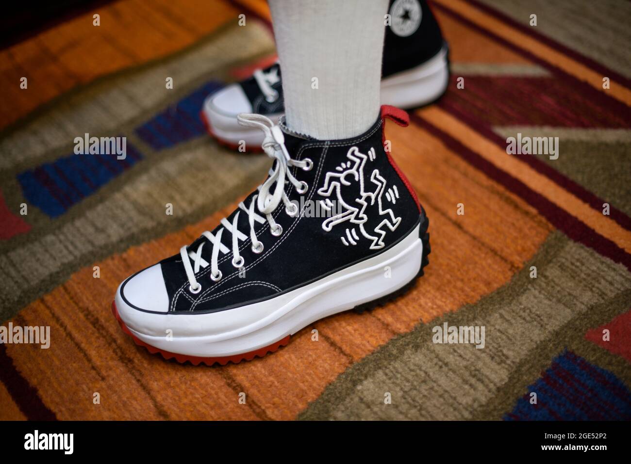 Ein junger Mann trägt ein Paar Converse High-Top-Sneakers, die mit Zeichnungen des Künstlers Keith Haring verziert sind. Stockfoto